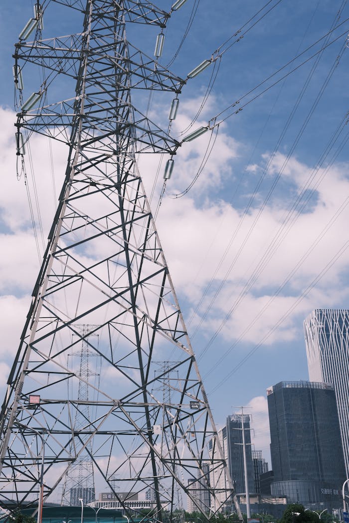 A towering electricity pylon against a city skyline with modern buildings and blue skies.