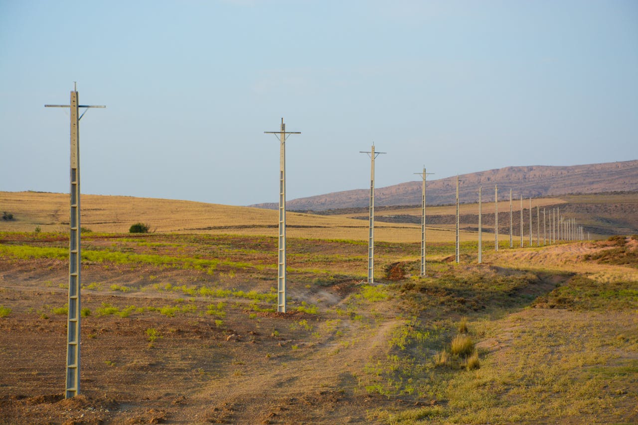 Lonely power lines navigate a dry, open field under a clear sky, highlighting technology in remote landscapes.